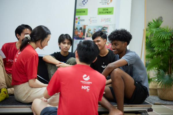 A group of volunteers and youths sitting in a circle and engaging in a conversation.