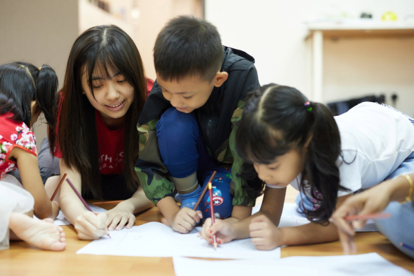 A volunteer engaging with a group of children through a writing activity.