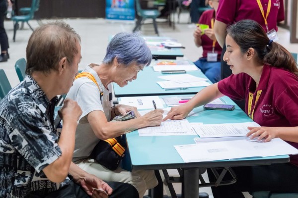 A volunteer going through a health screening questionnaire with two seniors.