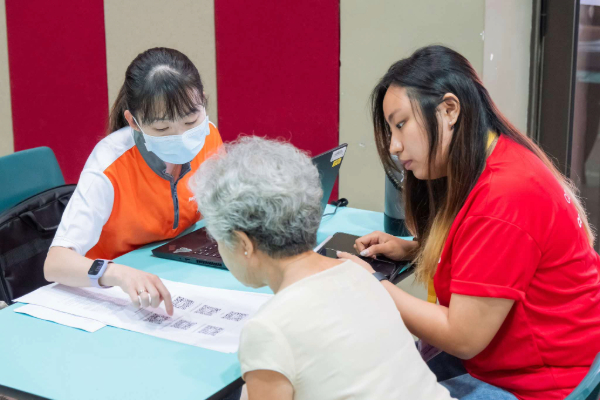 Two volunteers going through a health screening questionnaire with a senior.