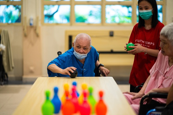 A senior keeping active by playing bowling with a volunteer.