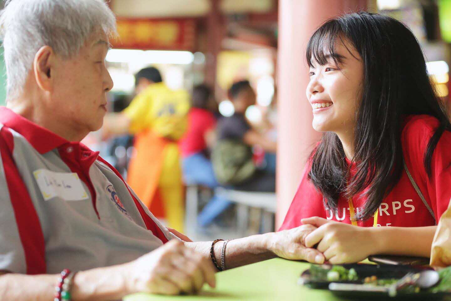 A volunteer engaging a senior while holding her hand.