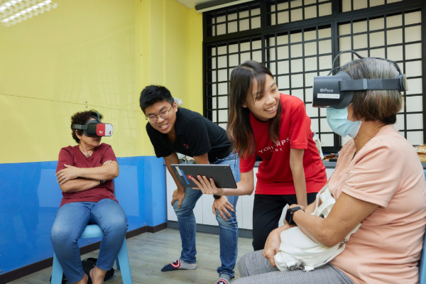 Two volunteers interacting with two seniors over the usage of Augmented Reality (AR) technology.